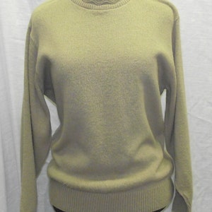 Puede incluir: Un suéter beige claro con cuello de canalé y mangas largas.