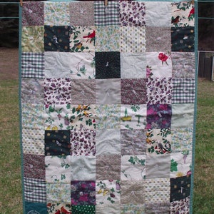 May include: A patchwork quilt with a variety of floral and bird patterns in shades of green, white, purple, and red. The quilt is made up of 25 squares and has a green border.