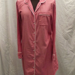 May include: A long-sleeved pink button-down shirt with white piping around the collar and cuffs. The shirt has a small pocket on the left chest.