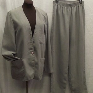 May include: A grey two-piece suit with a blazer and trousers. The blazer has a single button fastening and two pockets. The trousers have an elastic waistband and two pockets.