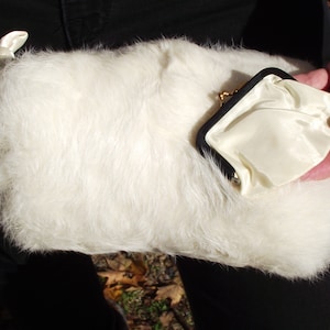 May include: A white fluffy clutch purse with a black and gold clasp. The purse is lined with a white satin fabric.