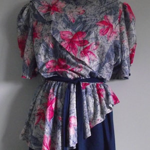 Può includere: Un abito vintage con la parte superiore a stampa floreale grigia e rosa e una gonna blu navy. La parte superiore ha un collo a volant e un laccio in vita.