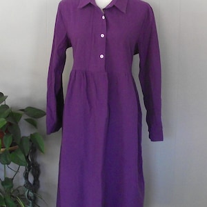 May include: A long-sleeved purple dress with a collared neckline and button closure. The dress has a slightly gathered waist and a straight skirt.