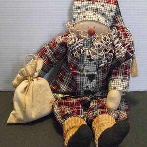 May include: A handmade rag doll dressed in red and black plaid pajamas with a white ruffle collar and a red and white plaid hat. The doll is holding a burlap sack.
