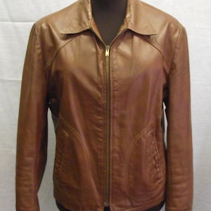 Op de afbeelding: Bruine leren jas met ritssluiting en kraag. De jas heeft twee voorzakken en wordt op een mannequin gepresenteerd. De jas heeft een bruine kleur.