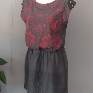 Könnte beinhalten: Ein graues, ärmelloses Kleid mit einem rosa floralen Stickmuster. Das Kleid hat eine Kordeltaille und einen gewellten Saum.