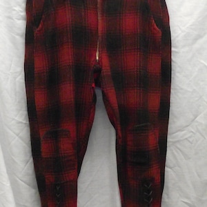 Puede incluir: Pantalones de cuadros rojos y negros con cremallera y detalles de encaje en la parte inferior de las piernas.