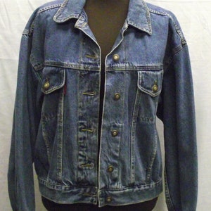 Op de afbeelding: Een blauw denim jack met een knoopsluiting en twee borstzakken.