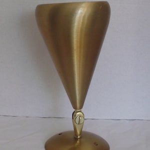 Może przedstawiać: Złota metalowa lampa z kloszem w kształcie stożka i okrągłą podstawą. Lampa ma jeden przełącznik z boku.