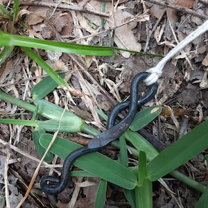 May include: A black metal hook with a loop on one end and a flat, curved piece on the other. The hook is attached to a white rope.