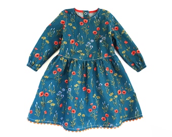 May include: A teal blue dress with a floral print of red poppies and other flowers. The dress has long sleeves and a round neckline. The hem of the dress is trimmed with a scalloped orange trim.
