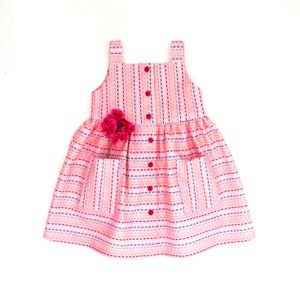 May include: A pink and white striped sleeveless dress with a button-up front and two pockets. The dress has a ruffled skirt and is decorated with colorful stitching.
