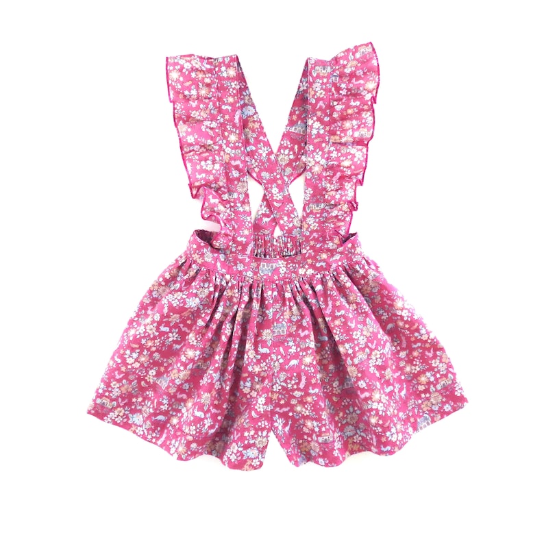 May include: A pink floral print overall dress with ruffled straps. The dress has a gathered skirt and a criss-cross strap design in the back.