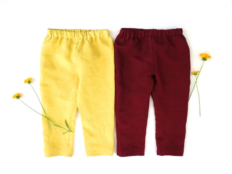 Puede incluir: Dos pares de pantalones para ni&ntilde;os, uno amarillo y otro burdeos. Los pantalones est&aacute;n colocados sobre un fondo blanco.