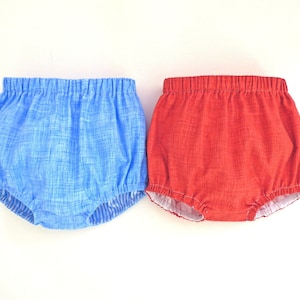 May include: Two pairs of baby bloomers, one blue and one red. The bloomers are made of a soft, textured fabric.