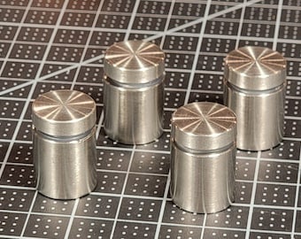 May include: Four silver metal standoffs with a decorative, circular, grooved top. The standoffs are on a black and white grid surface.