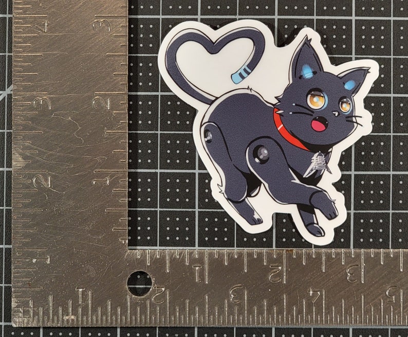 May include: A black and white cartoon sticker of a robot cat with a red collar and a heart-shaped tail. The cat has blue eyes and a surprised expression.