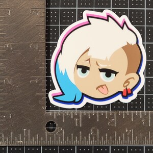 May include: A sticker of a cartoon character with white hair, blue eyes, and a tongue sticking out. The character is wearing red earrings and has a pink and blue outline.