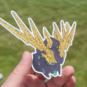 Peut inclure: Un autocollant de personnage d'anime doré et violet avec un design détaillé. Le personnage a une grosse tête avec une couronne dorée et un visage pointu et acéré.