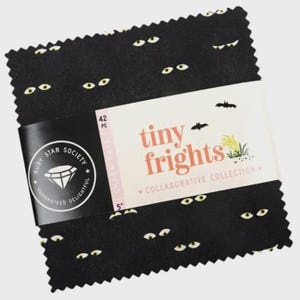 May include: A stack of 42 fabric squares measuring 5 inches each, featuring a black background with a repeating pattern of yellow eyes. A paper band wraps around the centre, labelled Tiny Frights, Ruby Star Society, and 42 PC Charm Pack.