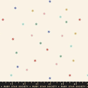 May include: Cream-colored fabric with a scattered pattern of colorful asterisks. The asterisks are in various colors, including red, blue, green, pink, and gold. The fabric has a ruler at the bottom with the text "RUBY STAR SOCIETY".