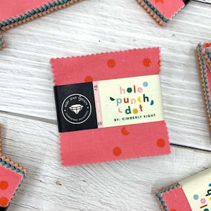 May include: A stack of pink fabric squares with red polka dots, wrapped with a label that reads "hole punch, dot" by Kimberly Kight. The label also features the Ruby Star Society logo and the text "Guaranteed Delightful". Each square measures 6.35 cm.