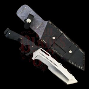 Puede incluir: Un cuchillo de acero inoxidable con mango negro y borde dentado, acompañado de una funda de cuero negro. La hoja plateada del cuchillo presenta un diseño único, sobre un fondo negro.