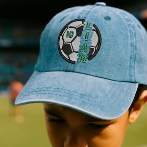 K&ouml;nnte beinhalten: Hellblaue Baseballkappe mit Fu&szlig;ball-Design. Der Fu&szlig;ball hat die Nummer 10 und den Namen "LIAM" in Gr&uuml;n und Schwarz aufgestickt. Die Kappe ist aus einem weichen Material.