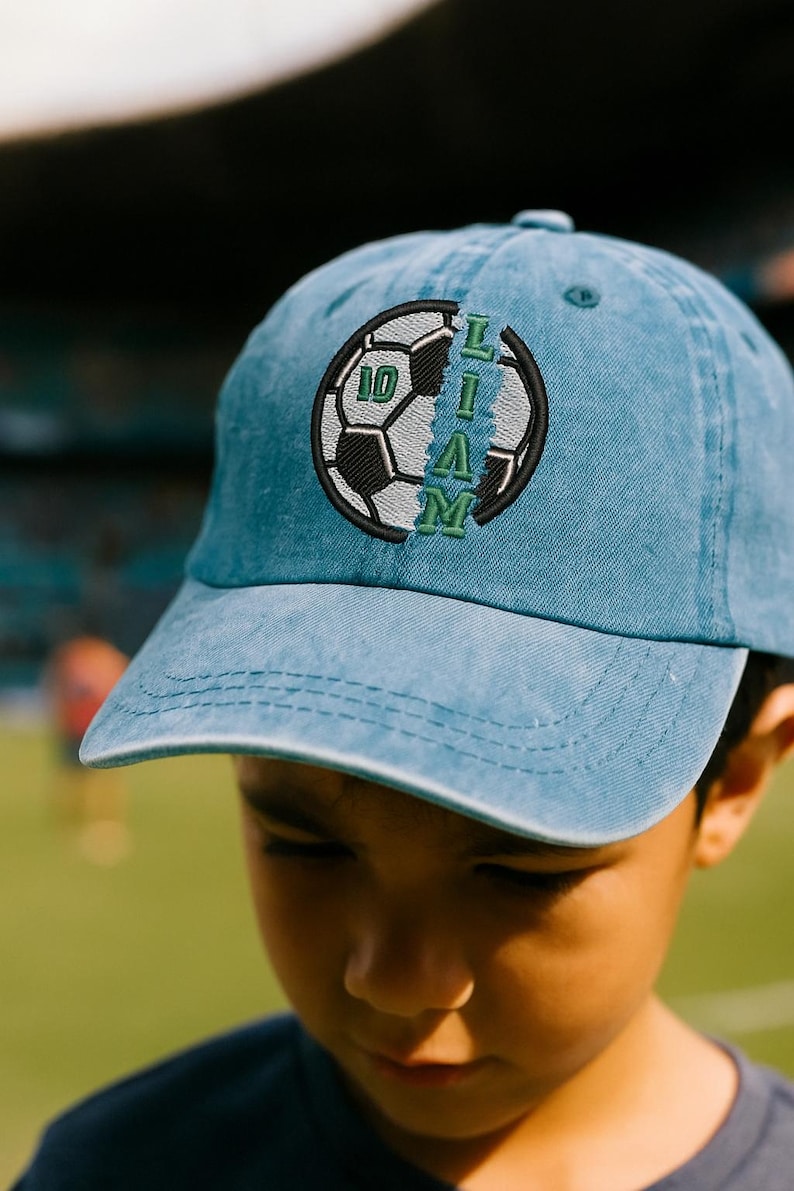 K&ouml;nnte beinhalten: Hellblaue Baseballkappe mit Fu&szlig;ball-Design. Der Fu&szlig;ball hat die Nummer 10 und den Namen "LIAM" in Gr&uuml;n und Schwarz aufgestickt. Die Kappe ist aus einem weichen Material.