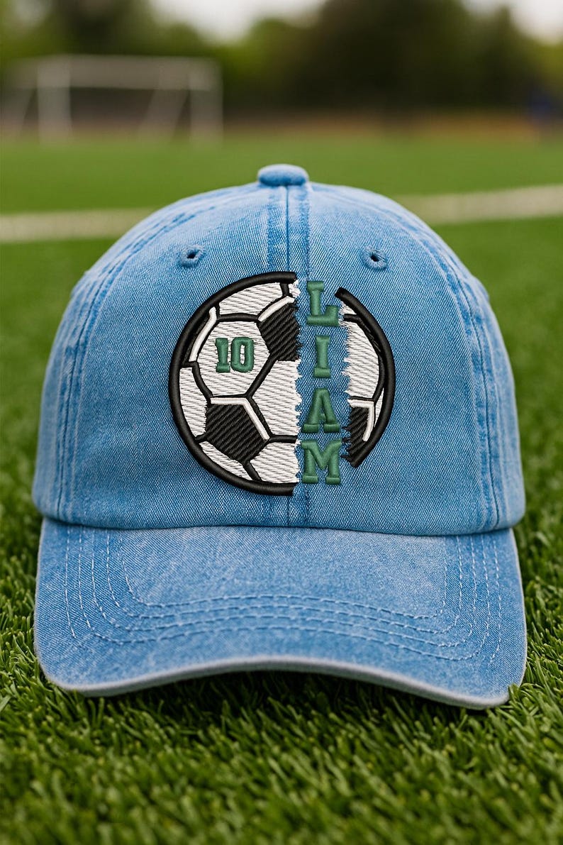 K&ouml;nnte beinhalten: Hellblaue Jeans-Baseballkappe mit einem Fu&szlig;ball-Design. Der Fu&szlig;ball ist schwarz und wei&szlig; mit dem Namen "LIAM" in gr&uuml;nen Buchstaben. Die Nummer "10" ist ebenfalls gr&uuml;n. Die Kappe befindet sich auf einem gr&uuml;nen Feld.