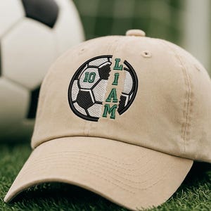 K&ouml;nnte beinhalten: Beige Baseball Cap mit einem Fu&szlig;ball-Design und dem Namen "LIAM" in gr&uuml;ner Schrift. Die Zahl "10" ist ebenfalls abgebildet. Im Hintergrund ist ein Fu&szlig;ball zu sehen.