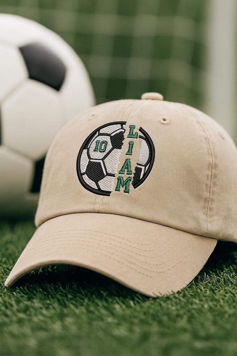 K&ouml;nnte beinhalten: Beige Baseball Cap mit einem Fu&szlig;ball-Design und dem Namen "LIAM" in gr&uuml;ner Schrift. Die Zahl "10" ist ebenfalls abgebildet. Im Hintergrund ist ein Fu&szlig;ball zu sehen.