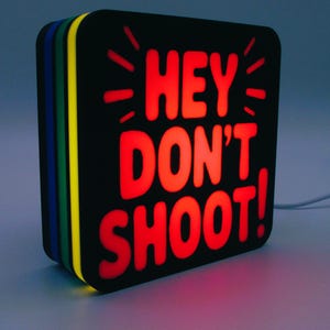 May include: A square, black light-up sign with rounded corners. The sign displays the red text "HEY DON'T SHOOT!" with radiating lines. The sides of the sign are layered with green, yellow, blue, and black.