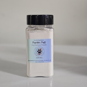 Könnte beinhalten: Eine transparente, rechteckige Flasche mit schwarzem Deckel, gefüllt mit weißem Pulver. Das Etikett lautet "Pawder Puff Dry Shampoo Powder" mit einem Pfotenabdruck-Logo. Zutaten: Pfeilwurzpulver, Maisstärke, Hafermehl und Kamille.