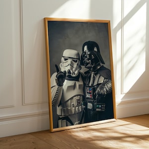 Puede incluir: Impresión enmarcada con los personajes Stormtrooper y Darth Vader. El Stormtrooper lleva un traje y casco blancos, haciendo el signo de la paz. Darth Vader lleva un traje y casco negros. La impresión está en un marco dorado.
