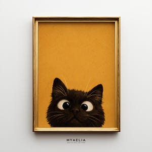 Può includere: Una stampa artistica incorniciata raffigurante un gatto nero con grandi occhi spalancati che sbuca dal bordo inferiore su uno sfondo giallo senape a tinta unita. La cornice è in oro metallizzato con un profilo sottile. Il testo MYAELIA è sotto.