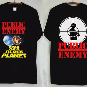 Könnte beinhalten: Schwarze T-Shirts mit Public Enemy-Grafiken. Eines zeigt "Public Enemy" über Planeten-Grafiken und "Fear of a Black Planet". Das andere zeigt ein Ziel-Grafik mit einer Silhouette und "Public Enemy" in Rot.