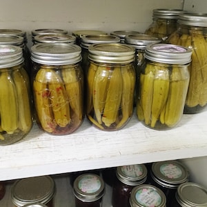 Peut inclure: Une étagère remplie de bocaux en verre d'okra marinée. Les bocaux sont disposés en rangées et sont tous remplis d'okra verte. Certains bocaux ont une teinte rouge au liquide.
