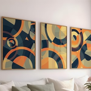 Può includere: Tre stampe artistiche astratte incorniciate. Ogni stampa presenta un design geometrico con archi e cerchi sovrapposti nei toni del blu navy, arancione e giallo. Le cornici sono dorate e l'opera d'arte è esposta sopra un divano bianco.