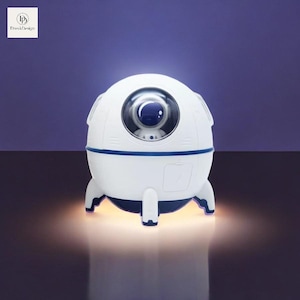 Könnte beinhalten: Ein weißes, astronautförmiges Nachtlicht mit einem blauen Visier und einer durchsichtigen Kuppel. Das Nachtlicht ist wie ein Raumschiff geformt mit drei Beinen und leuchtet in einem warmen Licht.