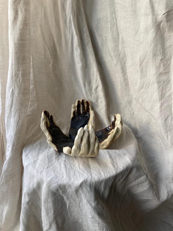 A ceramic sculpture of two open, outstretched hands — a timeless gesture rendered in hand-built clay with quiet emotional weight.