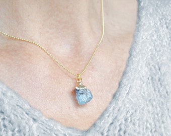May include: A gold chain necklace with a light blue gemstone pendant. The pendant is a rough, natural-looking stone.