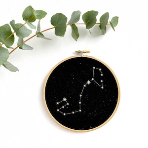 Peut inclure: Un cerceau de broderie noir avec une constellation de Sagittaire brodée en or sur un fond noir.