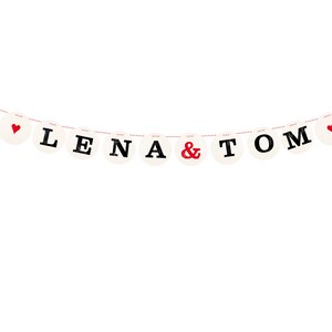 May include: A white banner with red hearts and black letters spelling "Lena & Tom" hanging on a red string.
