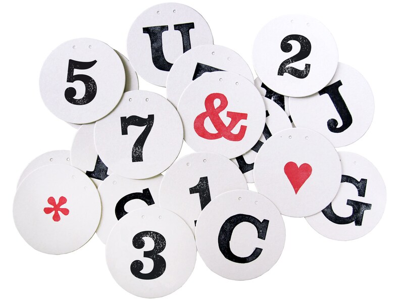 May include: A set of 14 round white paper tags with black and red lettering. The tags feature letters, numbers, and symbols, including an ampersand, a heart, and an asterisk.
