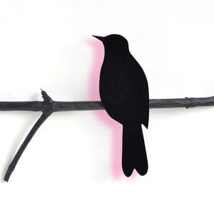 Könnte beinhalten: Schwarze Silhouette eines Vogels, der auf einem kahlen Zweig sitzt. Der Vogel schaut nach links und hat einen rosa Umriss.