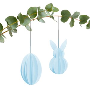 Könnte beinhalten: Zwei hellblaue Osterdekorationen aus Papier, die an einem Eukalyptuszweig hängen. Eine Dekoration ist eiförmig, die andere hat die Form eines Hasen.