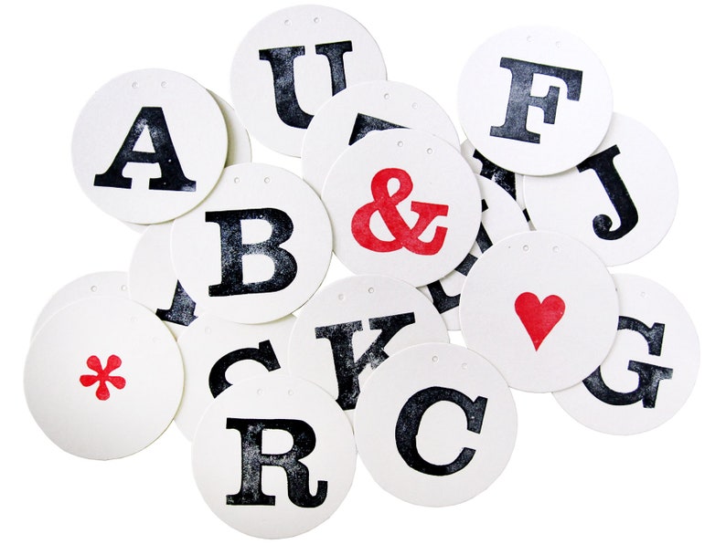 May include: A set of 13 white round paper circles with black letters and symbols, including A, B, C, F, G, J, K, R, U, and the ampersand symbol. One circle has a red asterisk, another has a red heart, and another has a red ampersand.