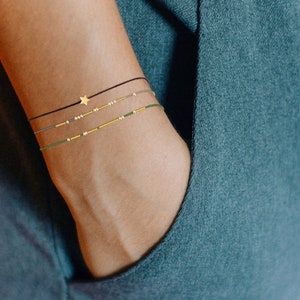 May include: Three layered anklets with a gold star charm. The anklets are black, green, and brown.