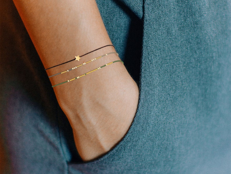 May include: Three layered anklets with a gold star charm. The anklets are black, green, and brown.